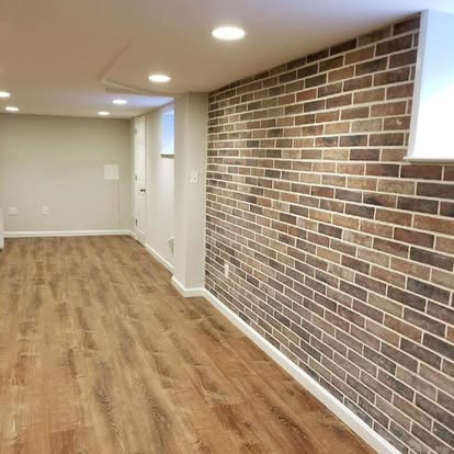 Modern basement finishing ideas with wood-look flooring, recessed lighting, and a brick accent wall