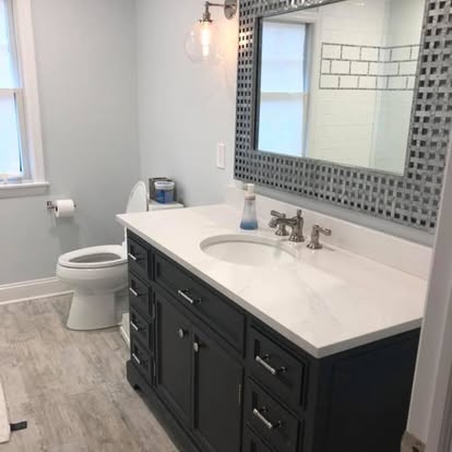 Luxury bathroom design ideas New Jersey with dark custom vanity, white countertop, large mirror, and modern fixtures